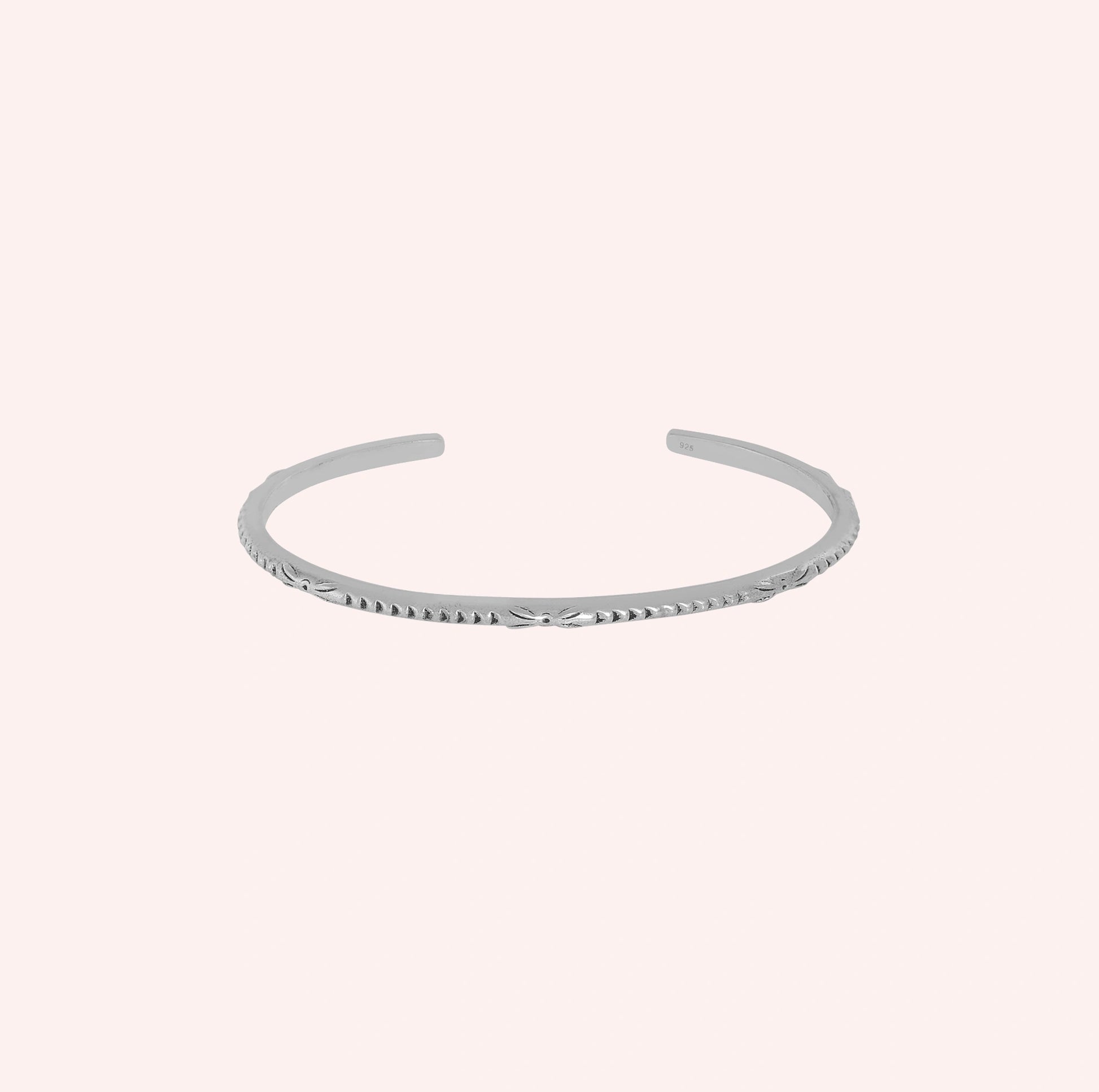 Sterling_silver_bracelet_with_engraved_design_at_front_angle_view_on_solid_pink_background