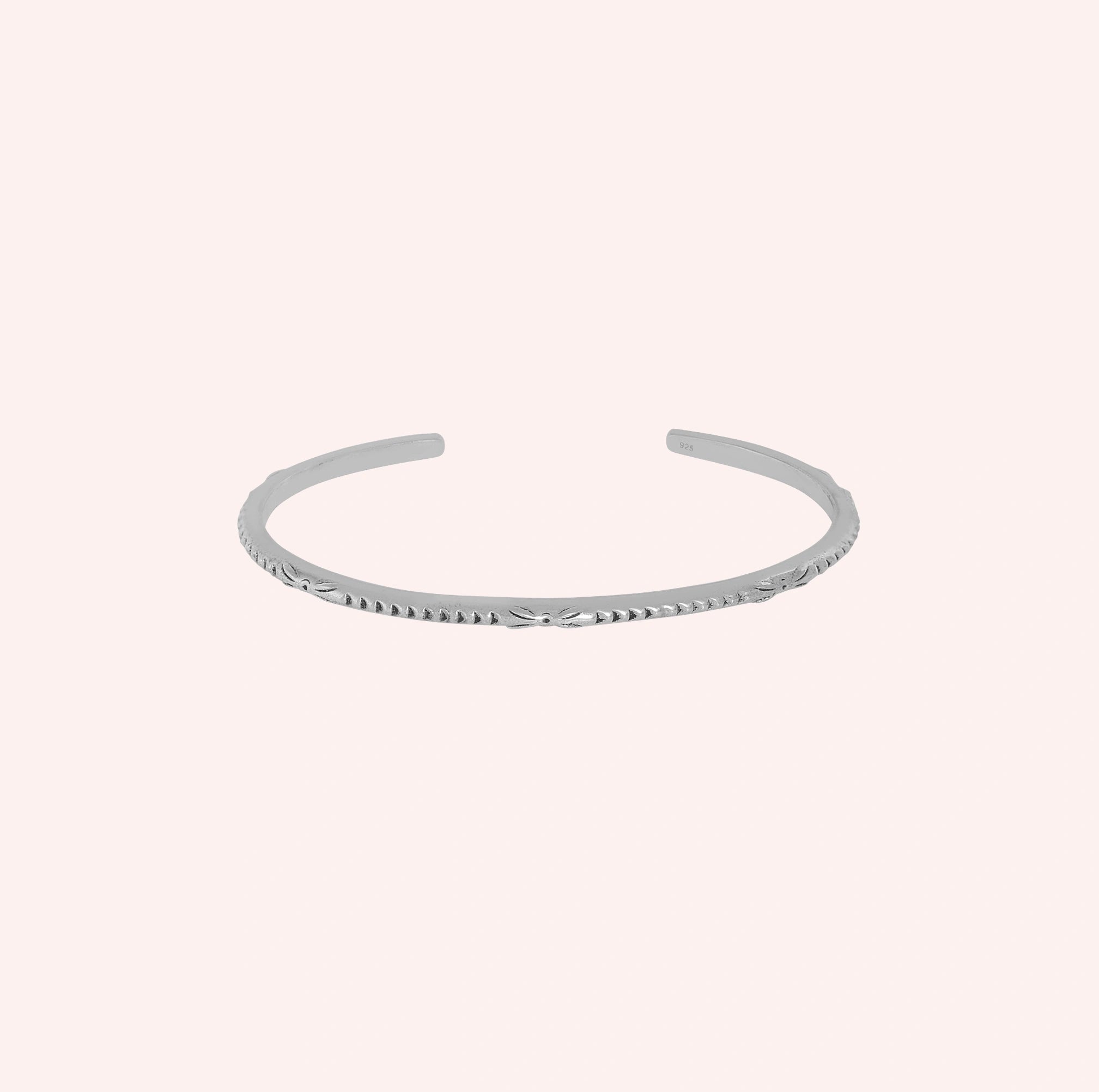 Sterling_silver_bracelet_with_engraved_design_at_front_angle_view_on_solid_pink_background