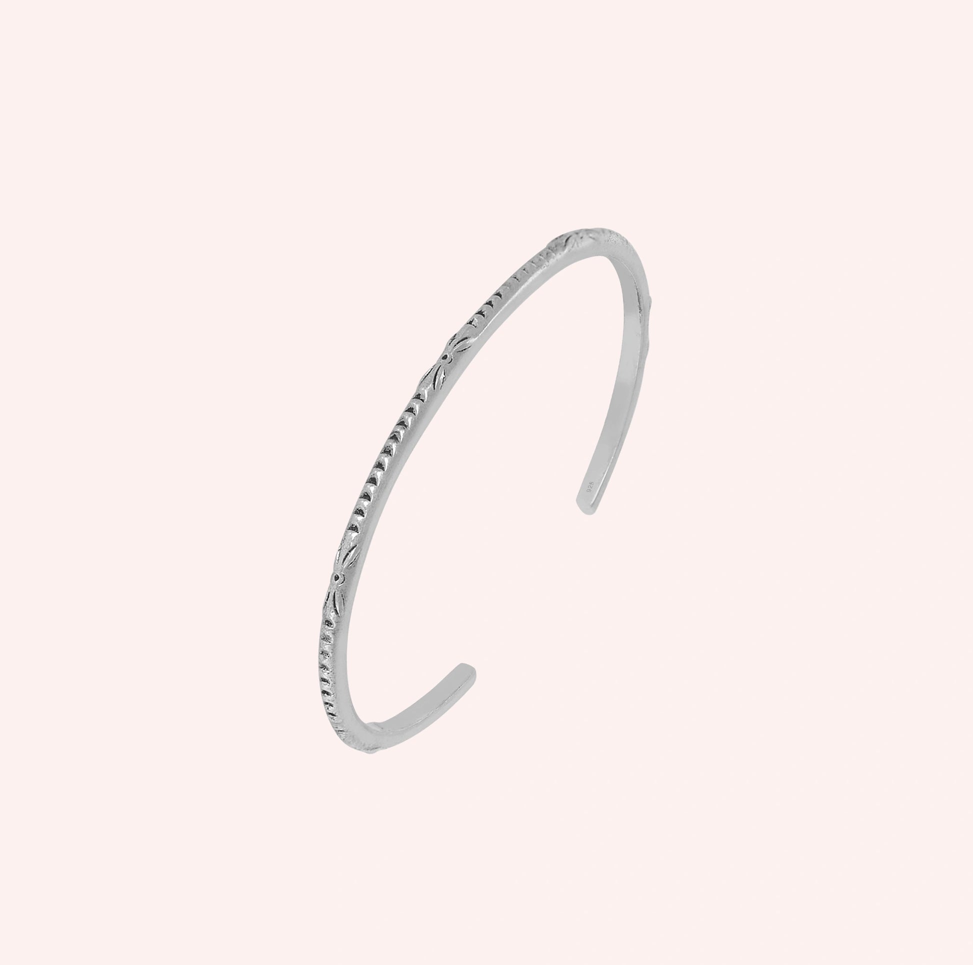 Sterling_silver_bracelet_with_engraved_design_at_slight_angle_view_on_solid_pink_background