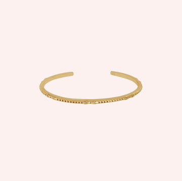 Sterling_silver_bracelet_in_gold_plated_silver_with_engraved_design_at_front_angle_view_on_solid_pink_background