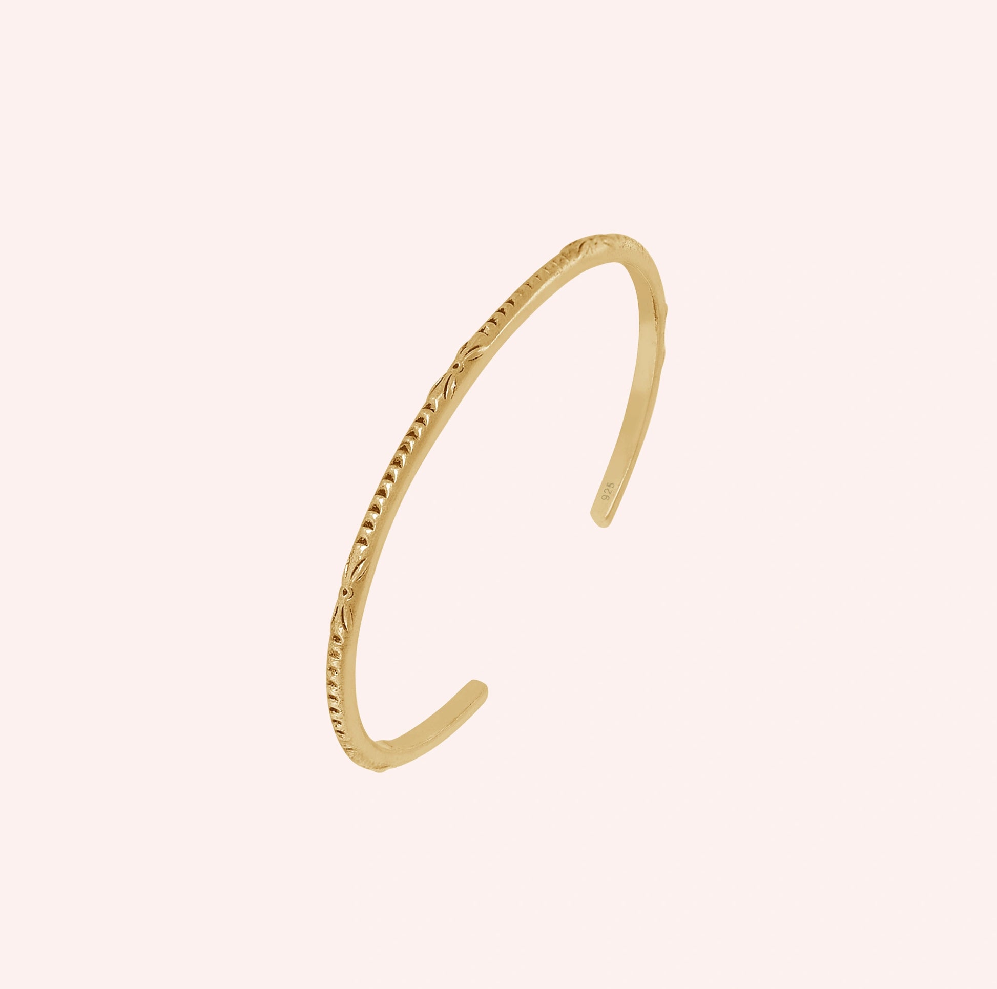 Sterling_silver_bracelet_in_gold_plated_silver_with_engraved_design_at_slight_angle_view_on_solid_pink_background