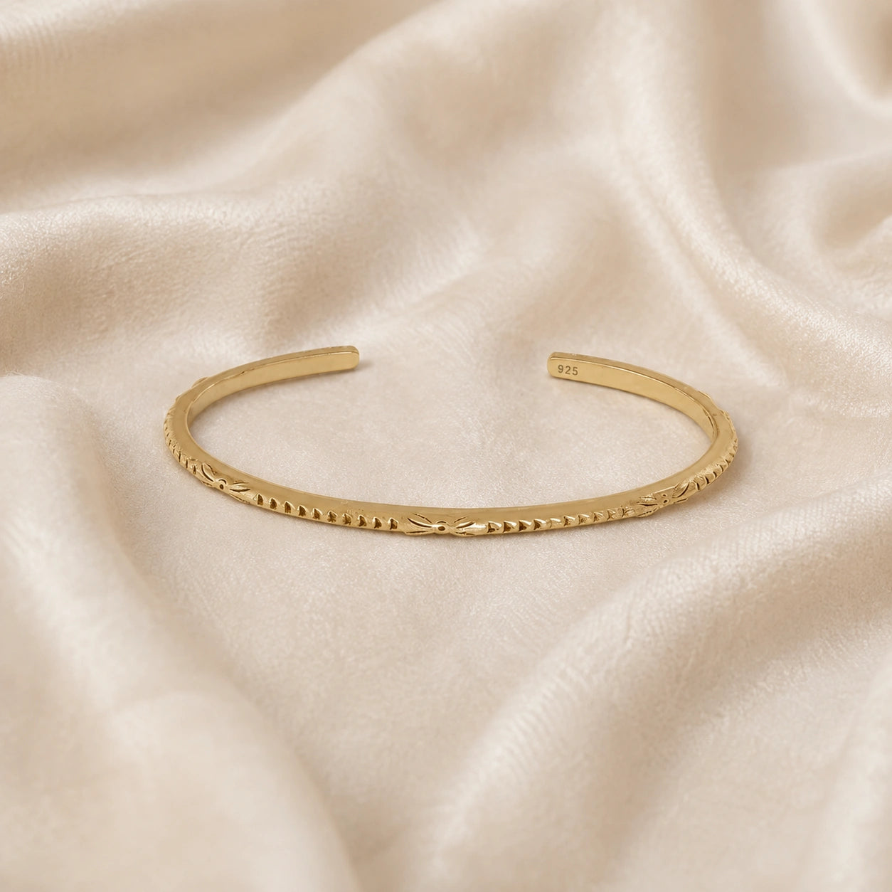 Sterling_silver_bracelet_in_gold_plated_silver_with_engraved_design_at_front_angle_view_on_soft_fabric_background
