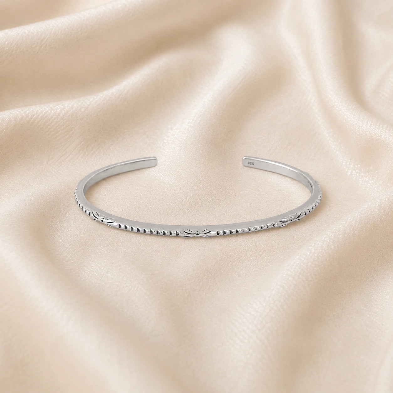 Sterling_silver_bracelet_in_sterling_silver_with_engraved_design_at_front_angle_view_on_soft_fabric_background