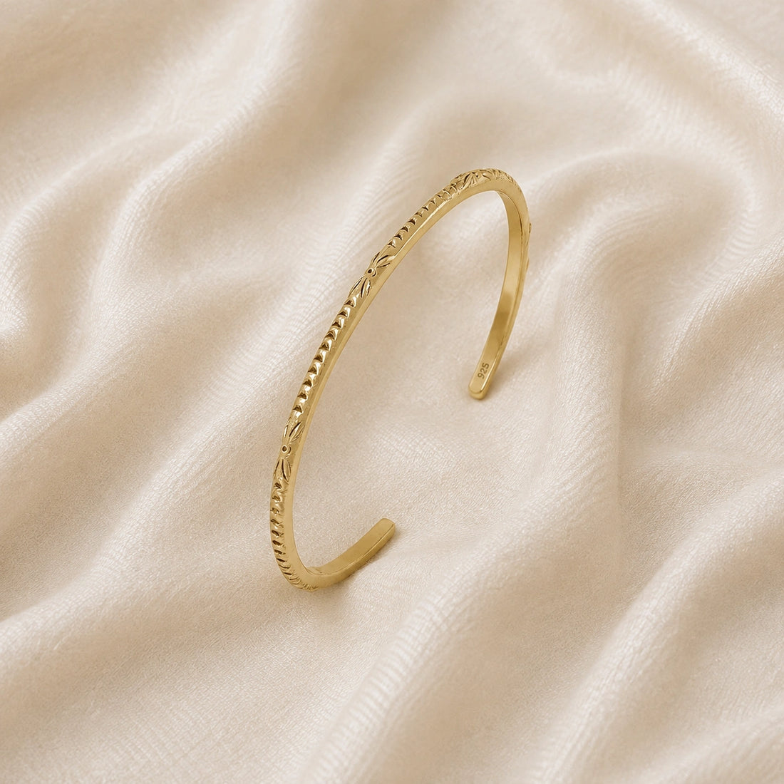 Sterling_silver_bracelet_in_gold_plated_silver_with_engraved_design_at_slight_angle_view_on_soft_fabric_background