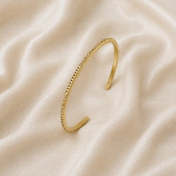 Sterling_silver_bracelet_in_gold_plated_silver_with_engraved_design_at_slight_angle_view_on_soft_fabric_background
