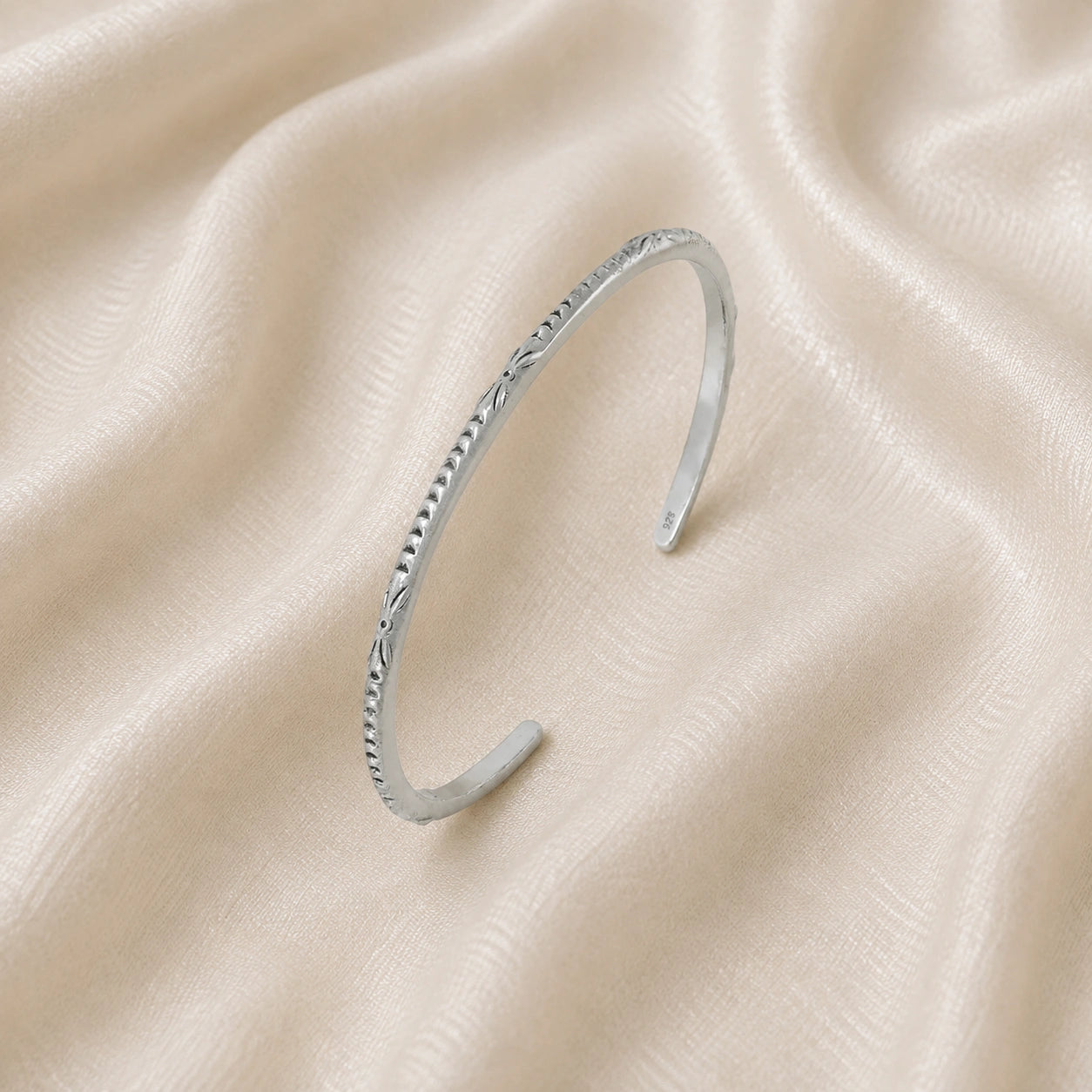 Sterling_silver_bracelet_in_sterling_silver_with_engraved_design_at_slight_angle_view_on_soft_fabric_background