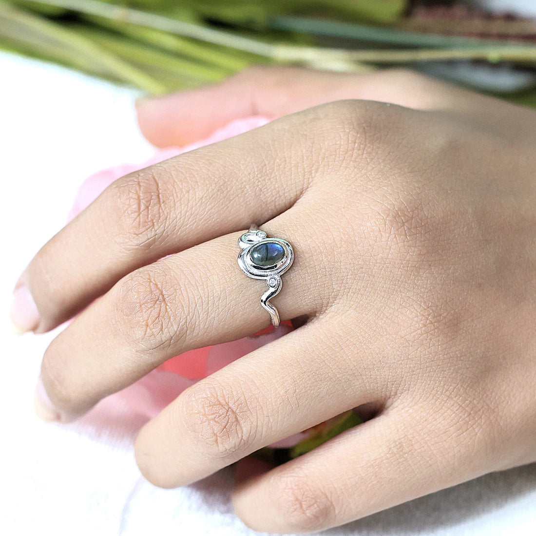 Front view of a sterling silver labradorite ring featuring an oval labradorite silver wavy ring band on white fabric background