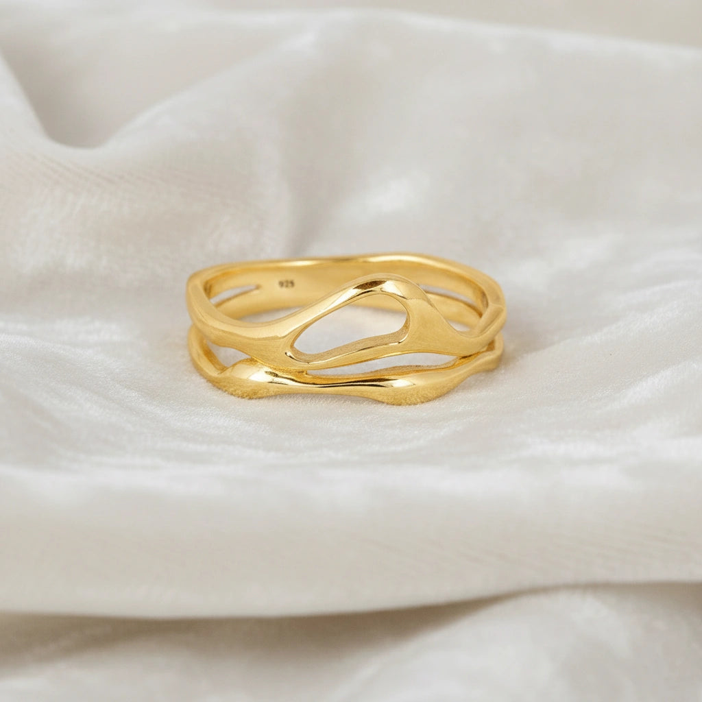 A gold vermeil wave band ring on white velvet shown from a front angle as a polished sterling silver rings for women's accessories