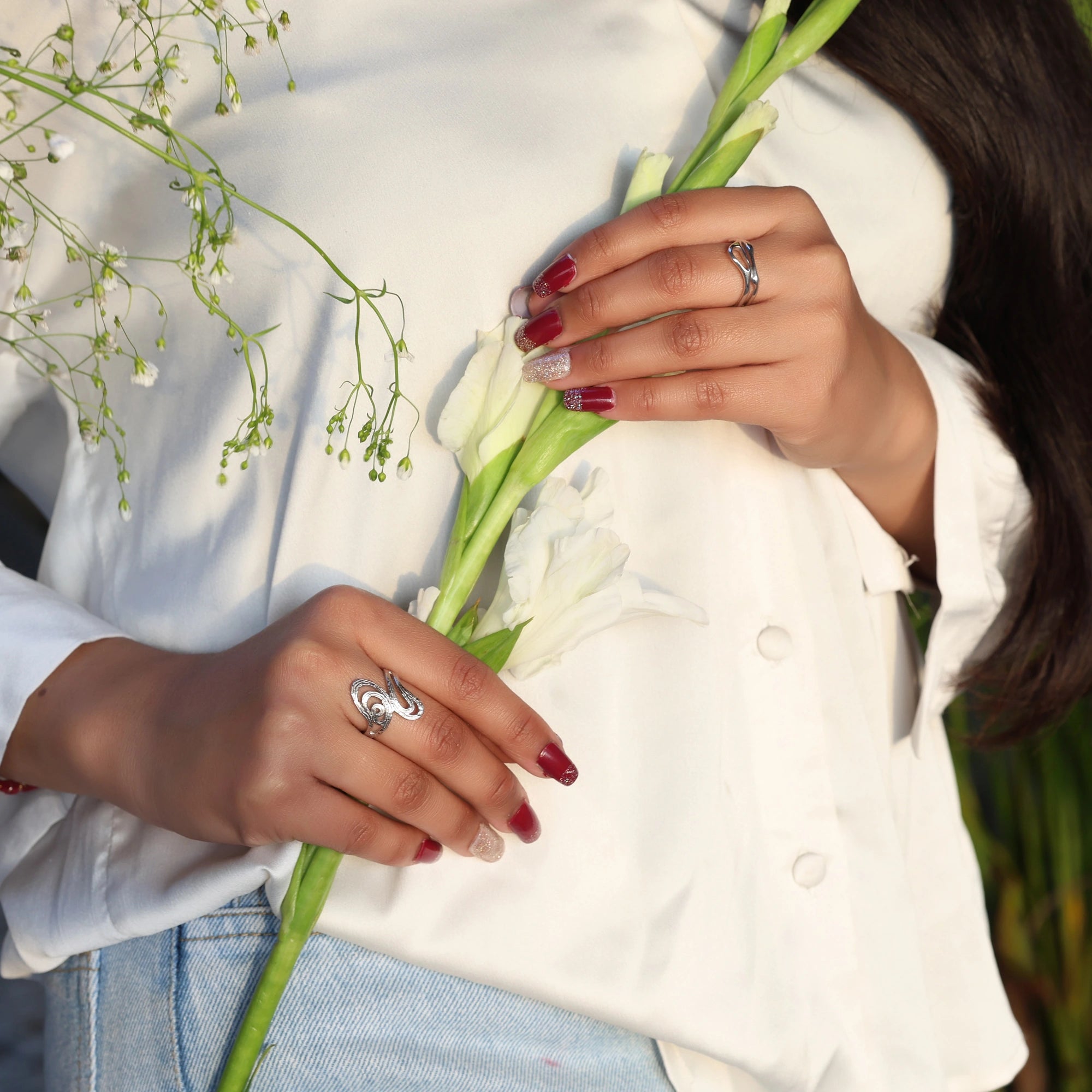 sterling silver rings for women wave band ring shown at a top angled view on both hands holding white flowers in natural light