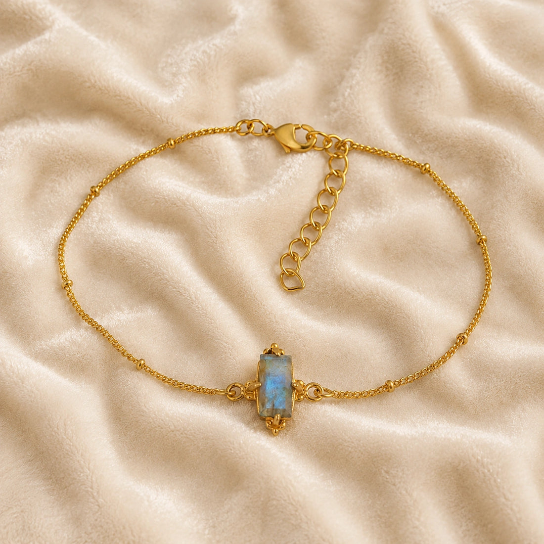 Stone_bracelet_in_gold_plated_silver_with_a_baguette_labradorite_at_front_angle_view_on_soft_fabric_background