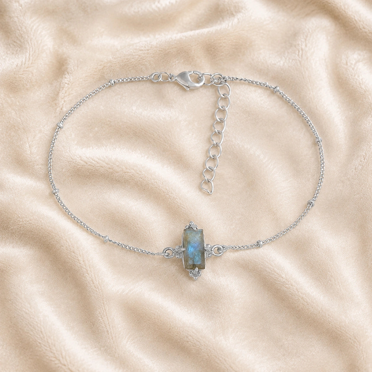 Stone_bracelet_in_sterling_silver_with_a_baguette_labradorite_at_front_angle_view_on_soft_fabric_background