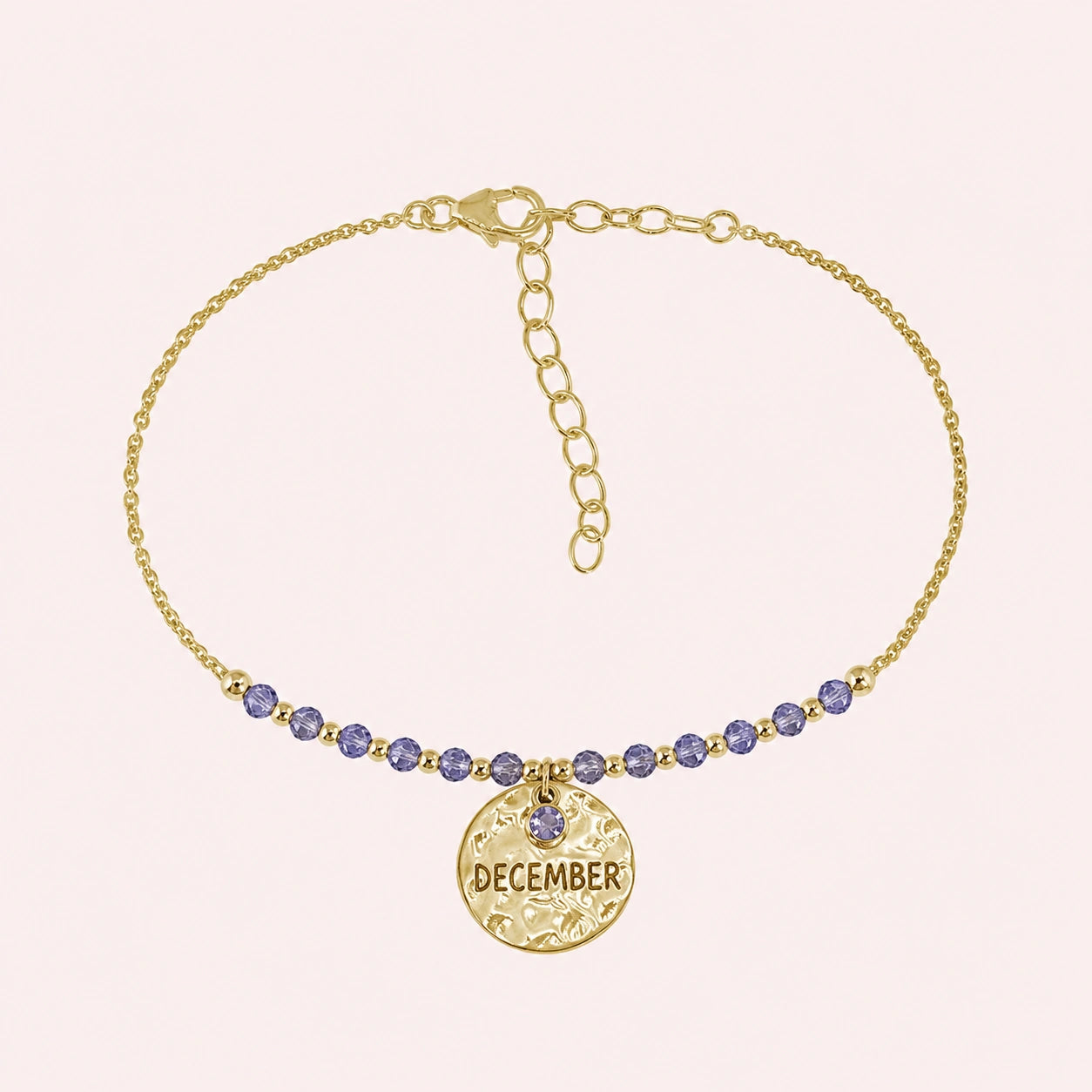 Birthstone_bracelet_in_gold_plated_silver_with_December_charm_and_tanzanite_beads_on_fine_chain_on_solid_pink_background