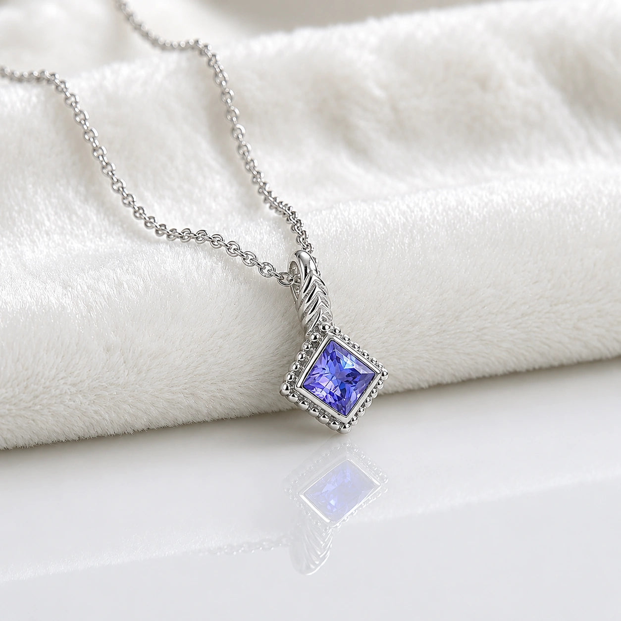 Birthstone_necklace_in_sterling_silver_with_square_cut_tanzanite_pendant_in_slightly_angled_view_on_soft_white_fabric_background