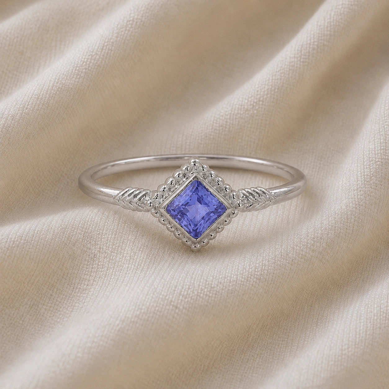 Princess_cut_ring_sterling_silver_with_square_tanzanite_and_detailed_band_front_angle_view_on_soft_fabric_background