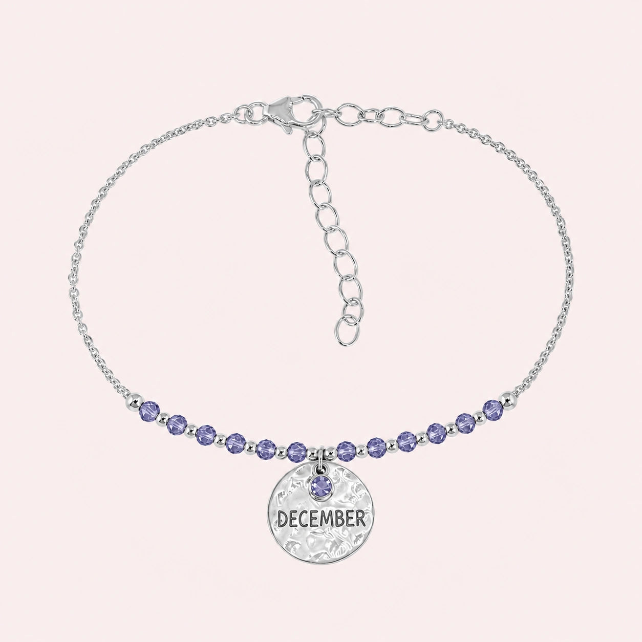 Birthstone_bracelet_in_sterling_silver_with_December_charm_and_tanzanite_beads_on_fine_chain_on_solid_pink_background