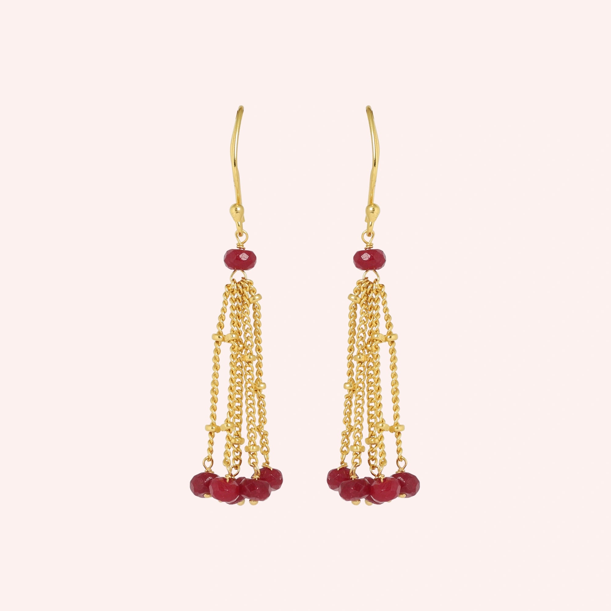 Tassel_earrings_in_gold_plated_silver_with_chain_and_ruby_stones_at_front_angle_view_on_solid_pink_background