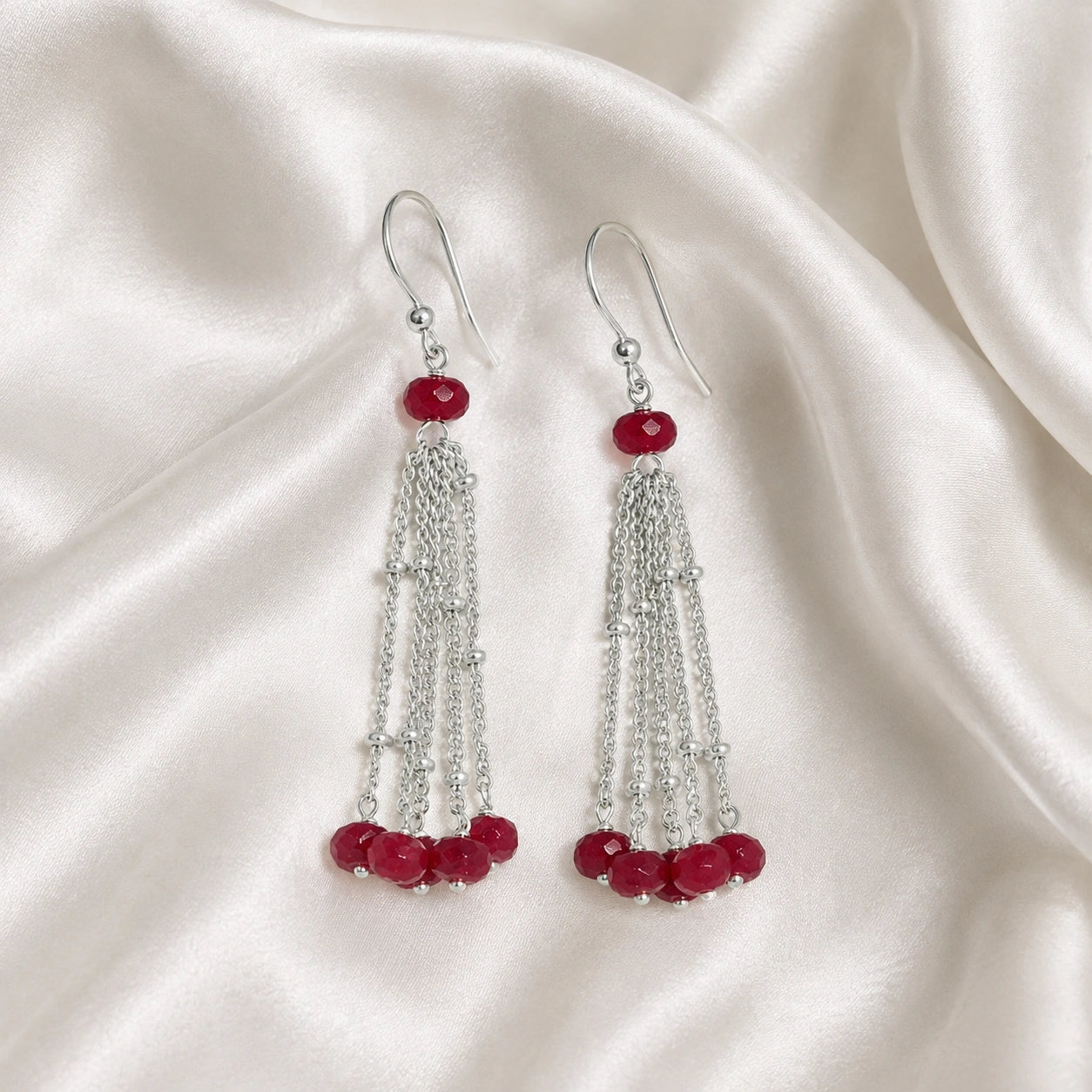Tassel_earrings_in_sterling_silver_with_chain_and_ruby_stones_at_slight_angle_view_on_soft_fabric_background