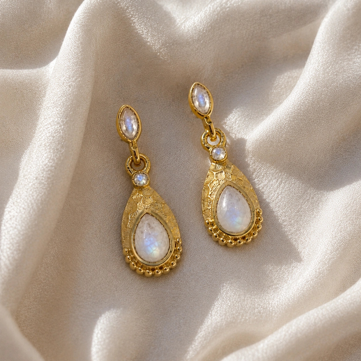 Teardrop_earrings_gold_plated_silver_with_moonstone_in_front_angled_view_on_soft_fabric_background