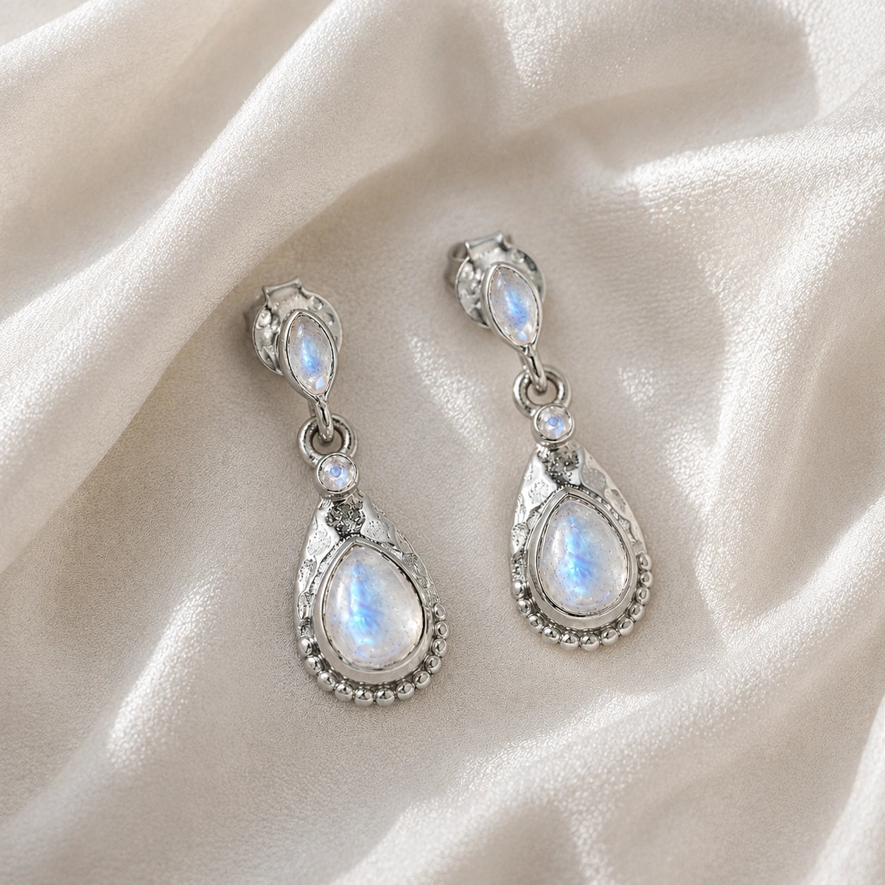 Teardrop_earrings_sterling_silver_with_moonstone_in_front_angled_view_on_soft_fabric_background
