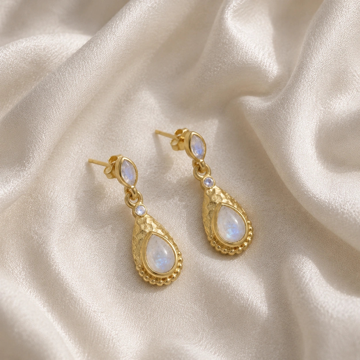 Teardrop_earrings_gold_plated_silver_with_moonstone_in_slightly_angled_view_on_soft_fabric_background