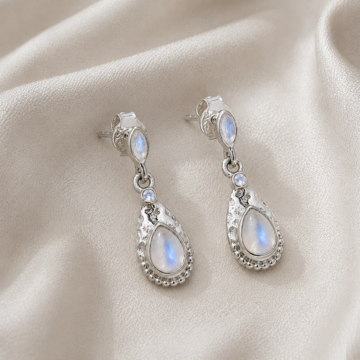 Teardrop_earrings_sterling_silver_with_moonstone_in_slightly_angled_view_on_soft_fabric_background