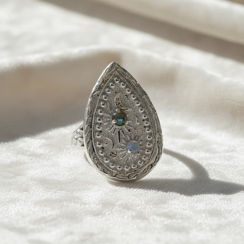 Celestial ring featuring a large teardrop silver design with carved sun moon and stars on a white cloth angled view