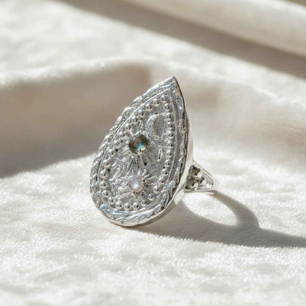 Celestial ring featuring a large teardrop with carved sun moon and stars on a white fabric background straight-on angle