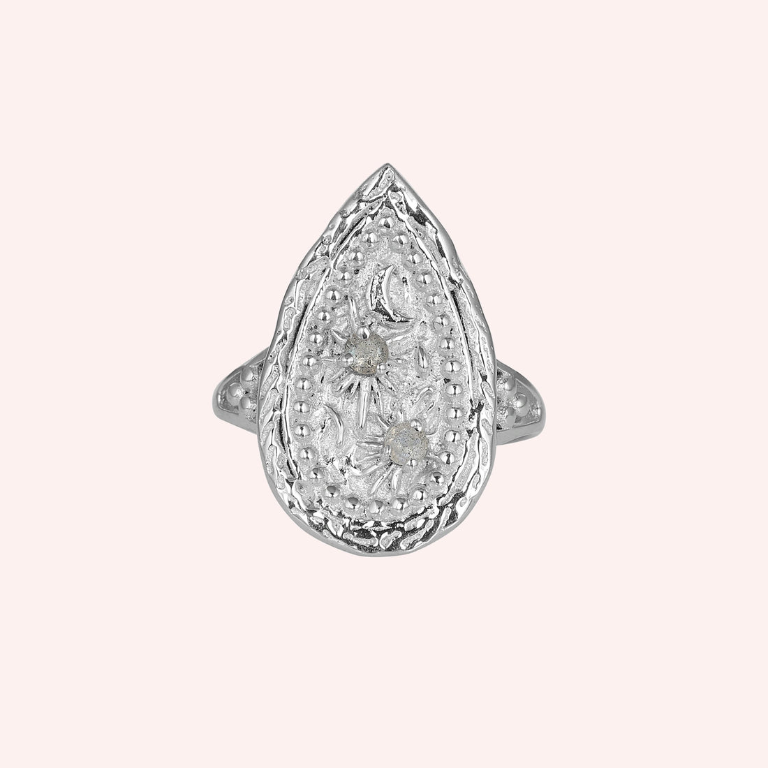 Celestial ring featuring a large teardrop silver design with carved sun moon and stars on a white cloth angled view