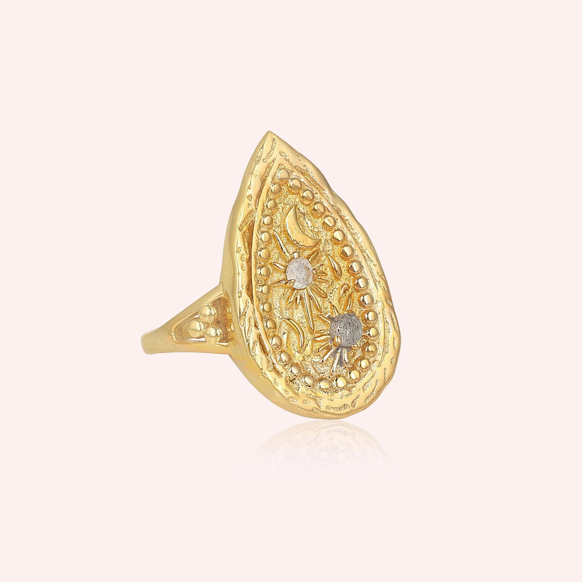 Gold plated celestial ring featuring a round labradorite stone on a pale pink background angled view