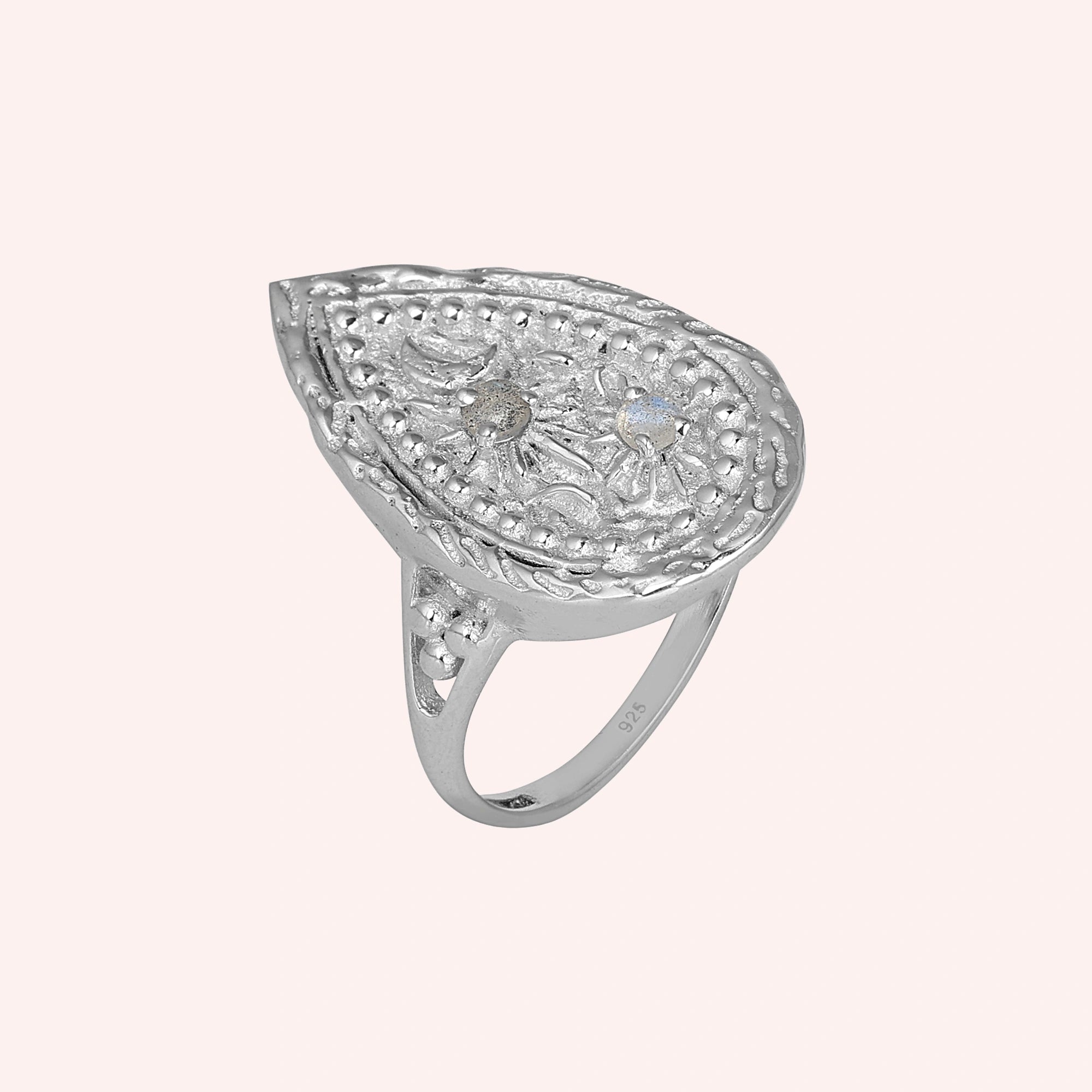 Celestial ring featuring a large teardrop silver design with carved moon and stars on a pale pink background slight right angle