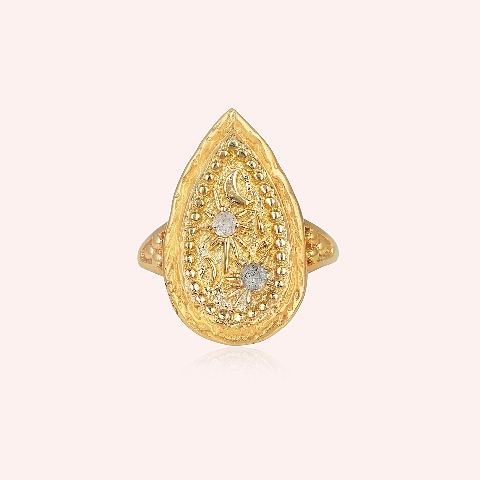 Gold plated celestial ring featuring a round labradorite stone and textured band on a pale pink background straight-on angle