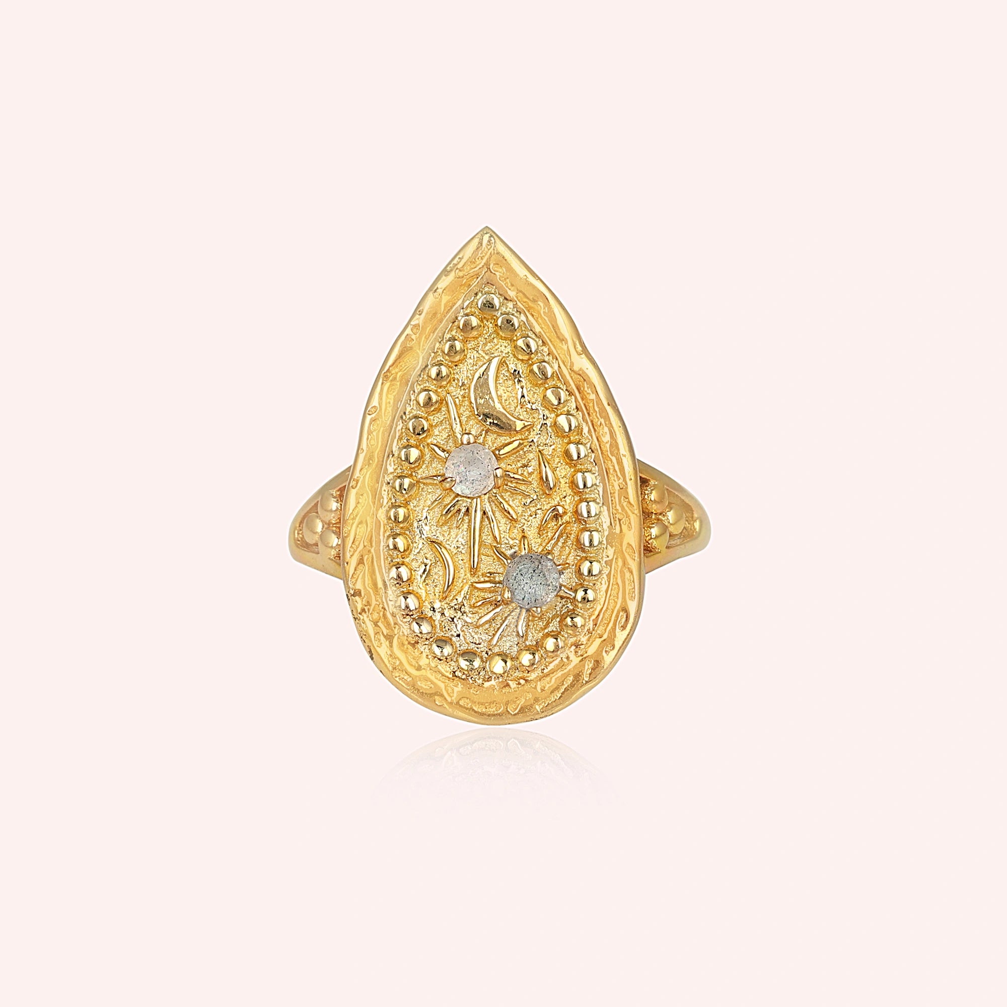 Gold plated celestial ring featuring a round labradorite stone and textured band on a pale pink background straight-on angle