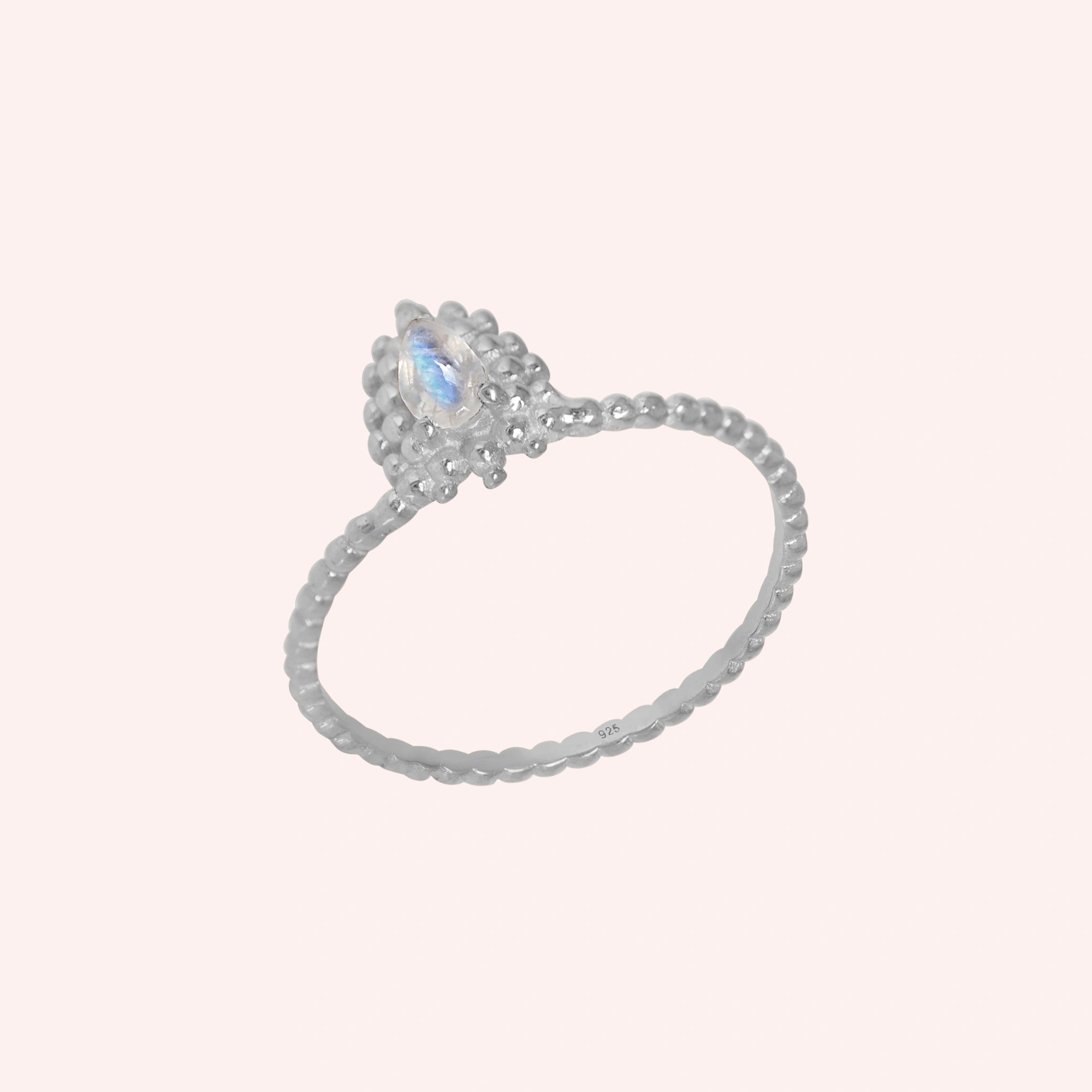 Teardrop_ring_sterling_silver_beaded_band_with_moonstone_at_tilted_angle_view_on_solid_pink_background