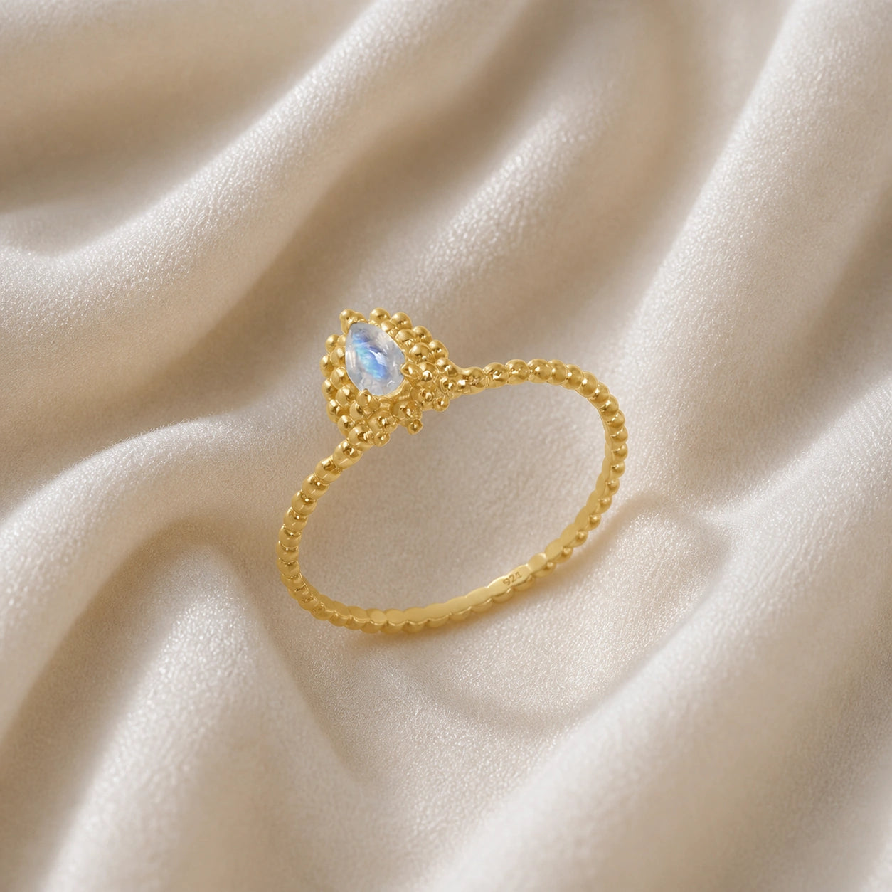Teardrop_ring_gold_plated_silver_beaded_band_with_moonstone_at_tilted_angle_view_on_soft_fabric_background