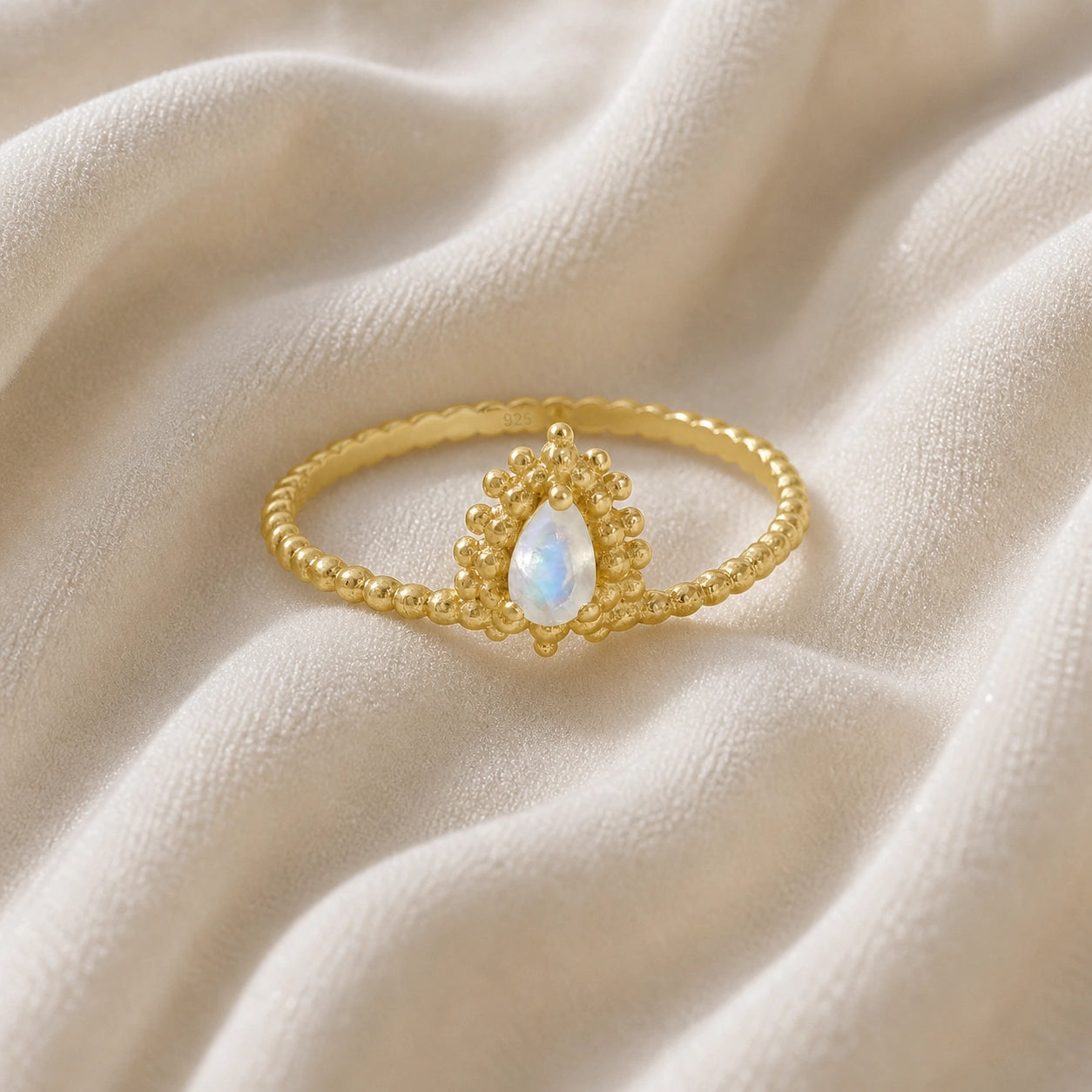 Teardrop_ring_gold_plated_silver_beaded_band_with_moonstone_at_front_angle_view_on_soft_fabric_background