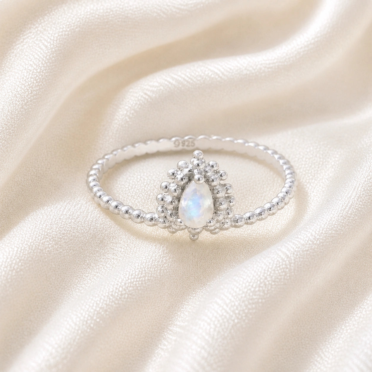 Teardrop_ring_sterling_silver_beaded_band_with_moonstone_at_front_angle_view_on_soft_fabric_background