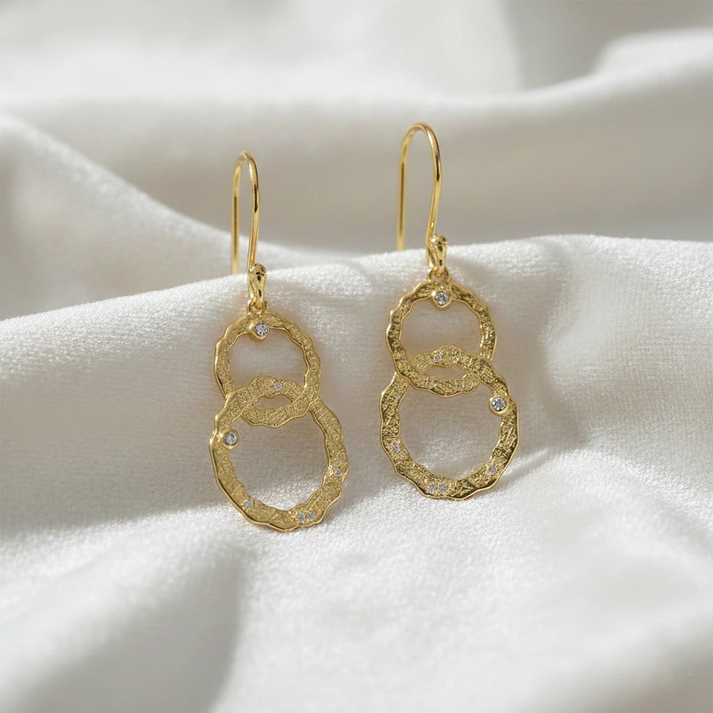 Gold-plated silver dangle earrings textured interlocking rings small labradorite stones slightly angled on a soft white fabric