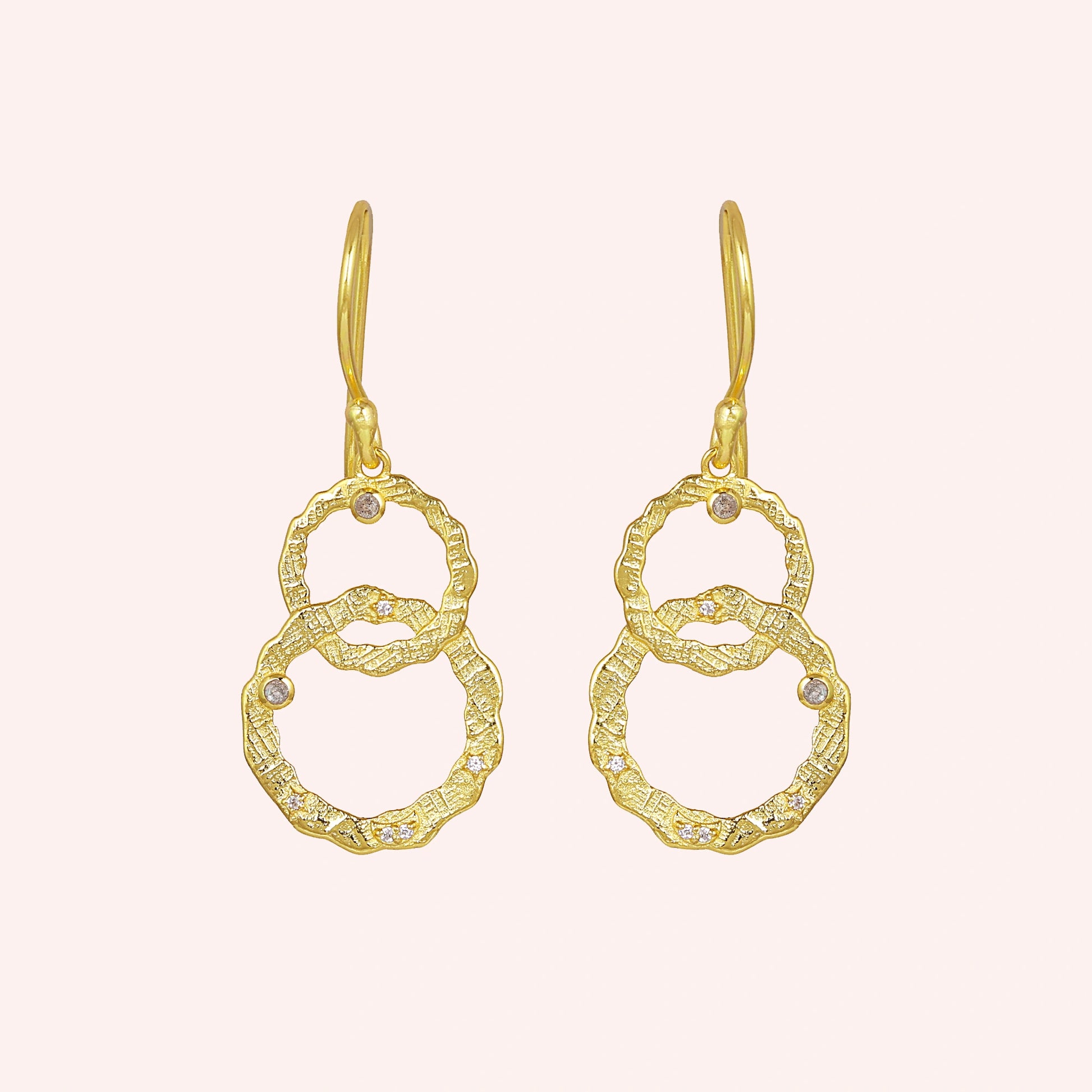 Gold plated silver dangle earrings textured interlocking rings with small labradorite stones viewed straight on a light pink surface