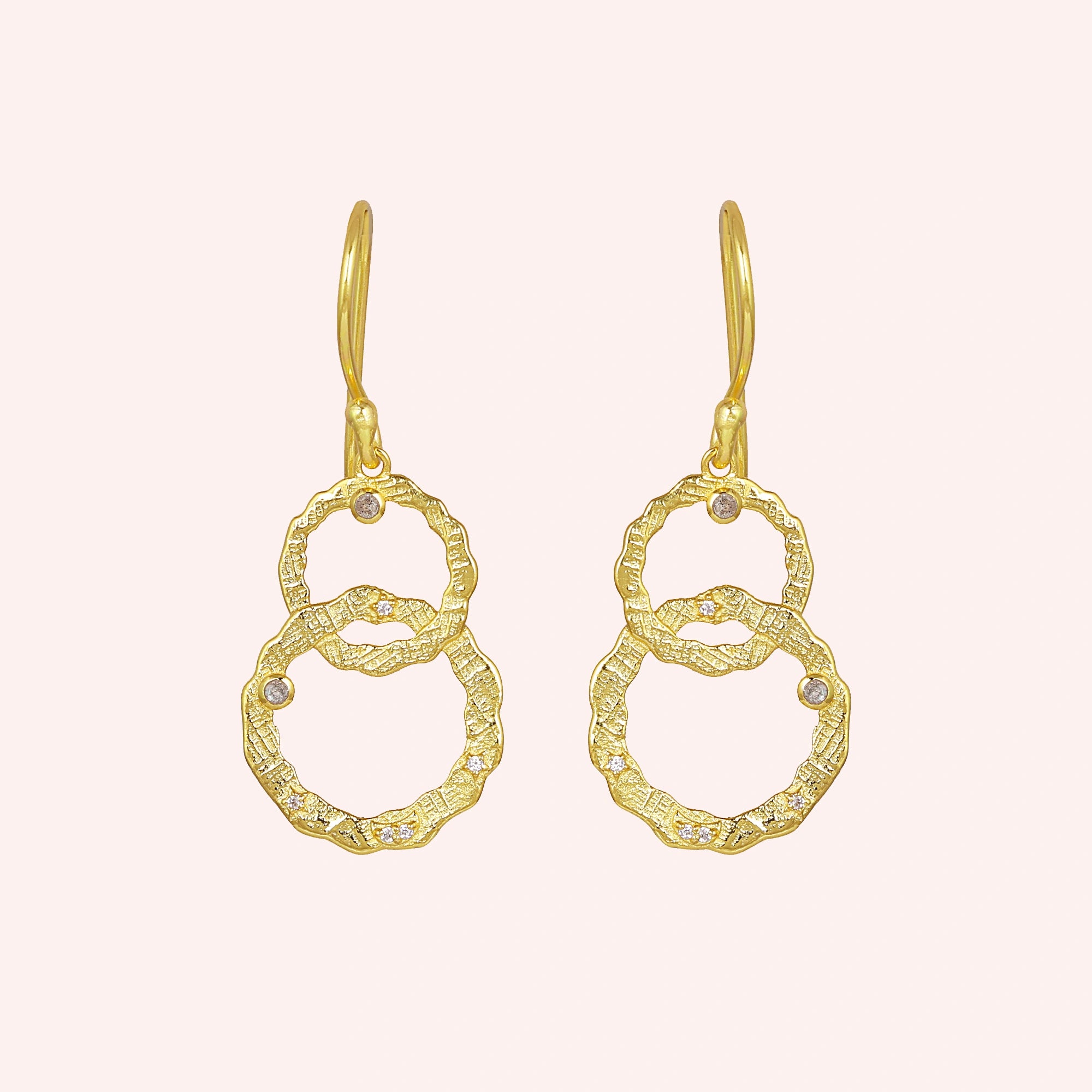 Gold plated silver dangle earrings textured interlocking rings with small labradorite stones viewed straight on a light pink surface
