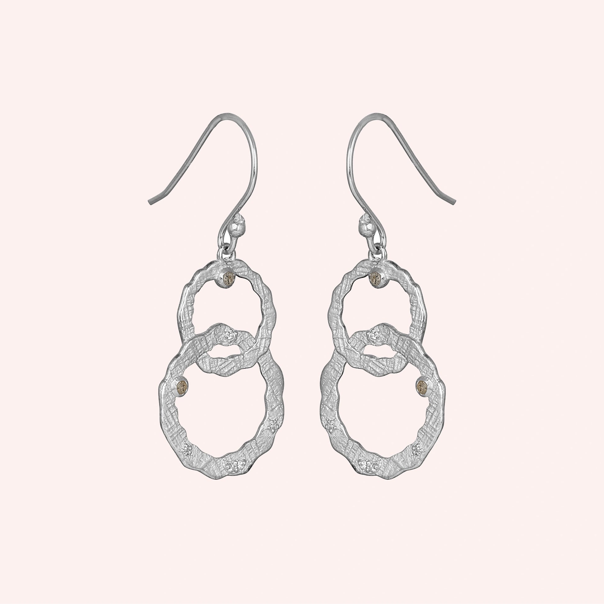 Silver dangle earrings textured interlocking rings with labradorite stones viewed straight on a light pink background