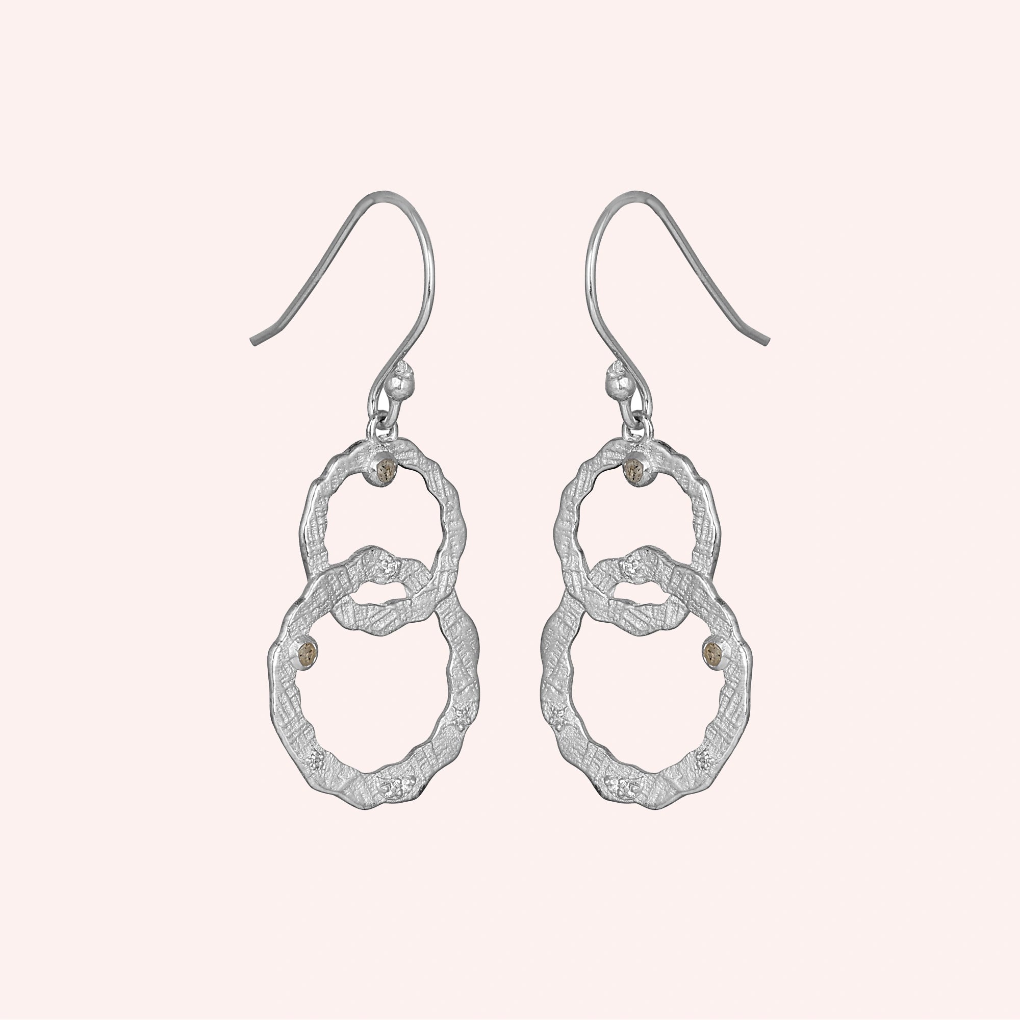 Silver dangle earrings textured interlocking rings with labradorite stones viewed straight on a light pink background