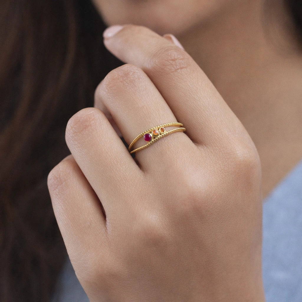 Three-stone-ring-worn-by-a-model-in-gold-plated-silver-with-pink-red-and-orange-stones-in-natual-light