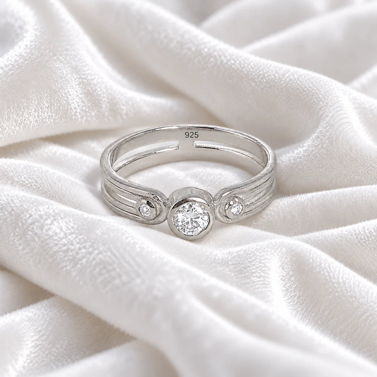Three_stone_ring_in_sterling_silver_with_round_lab_grown_diamonds_at_front_angle_view_on_soft_fabric_background