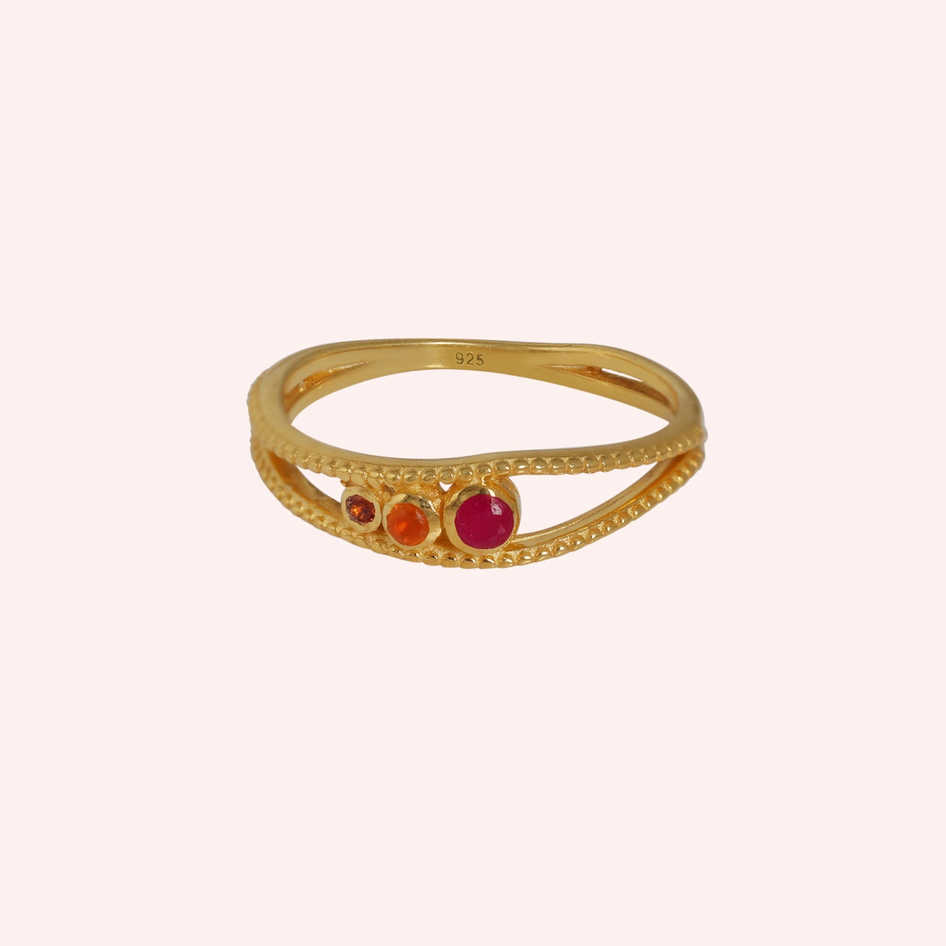 Three-stone-ring-in-gold-plated-silver-with-pink-red-and-orange-stones-in-front-view-on-solid-pinkbackground