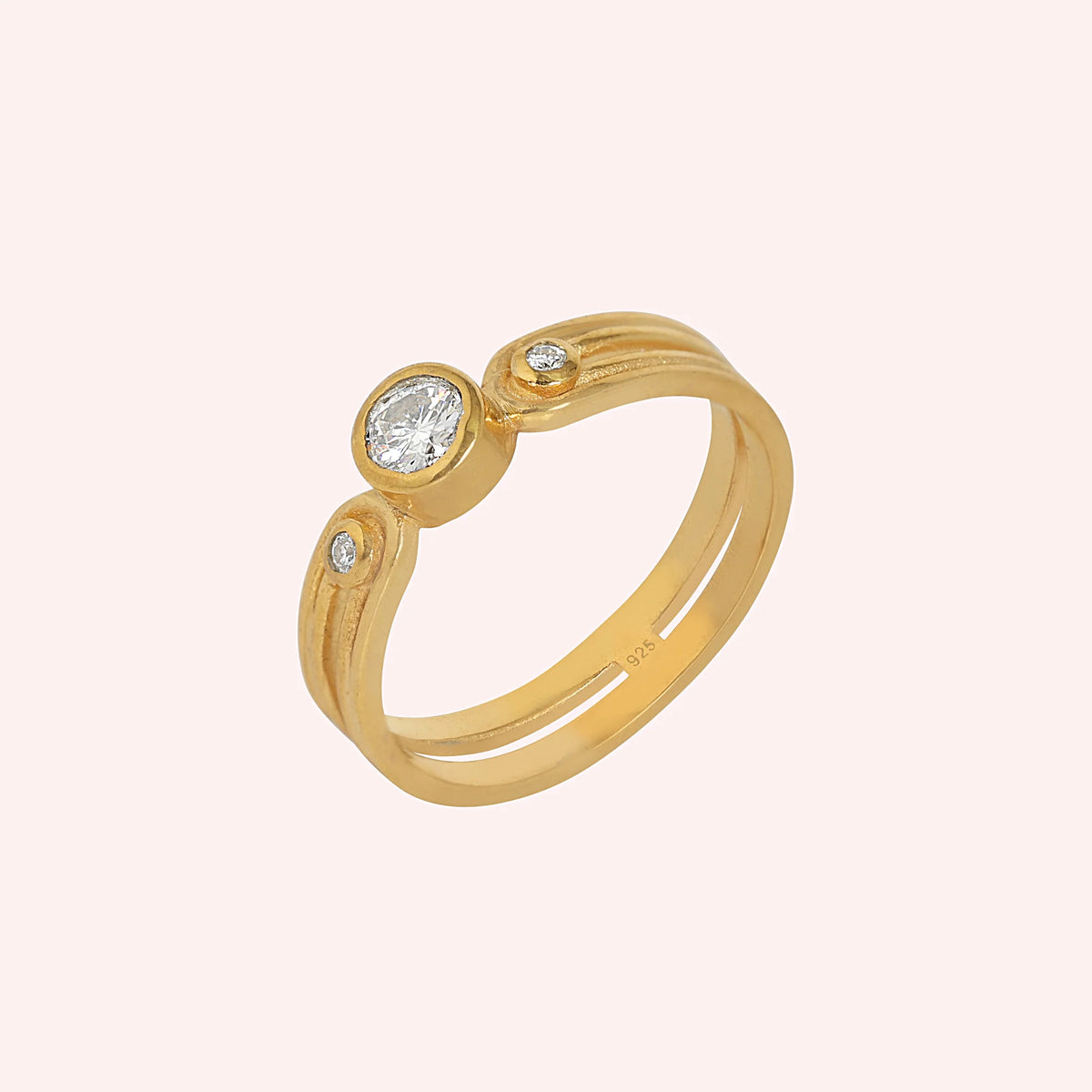 Three_stone_ring_in_gold_plated_silver_with_round_lab_grown_diamonds_at_side_angle_view_on_solid_pink_background
