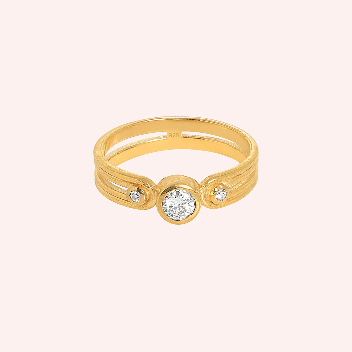 Three_stone_ring_in_gold_plated_silver_with_round_lab_grown_diamonds_at_front_angle_view_on_solid_pink_background