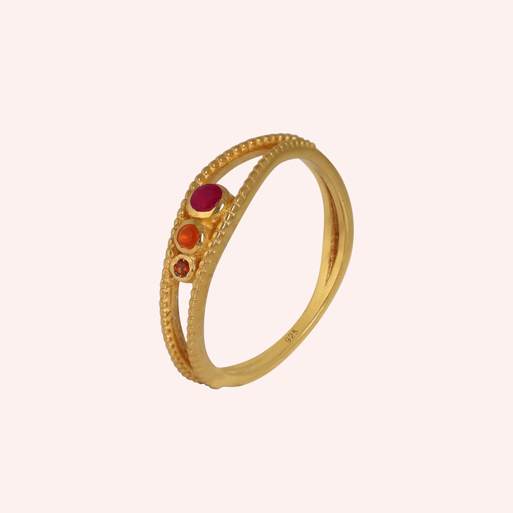 Three-stone-ring-in-gold-plated-silver-with-pink-red-and-orange-stones-in-angled-side-view-on-solid-pink-background