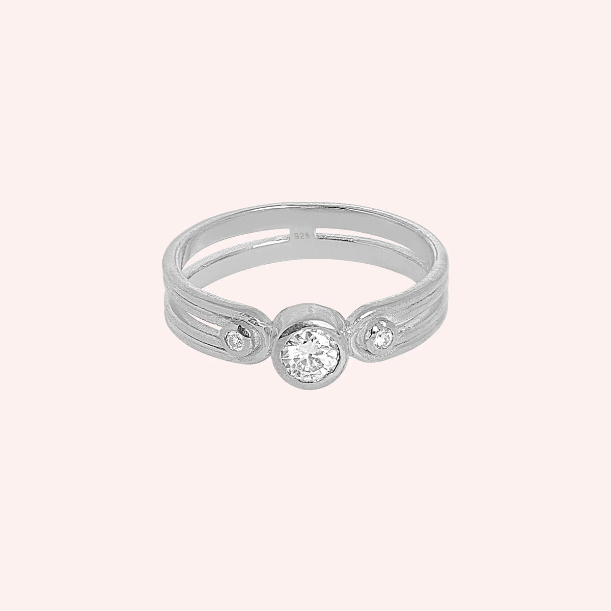 Three_stone_ring_in_sterling_silver_with_round_lab_grown_diamonds_at_front_angle_view_on_solid_pink_background