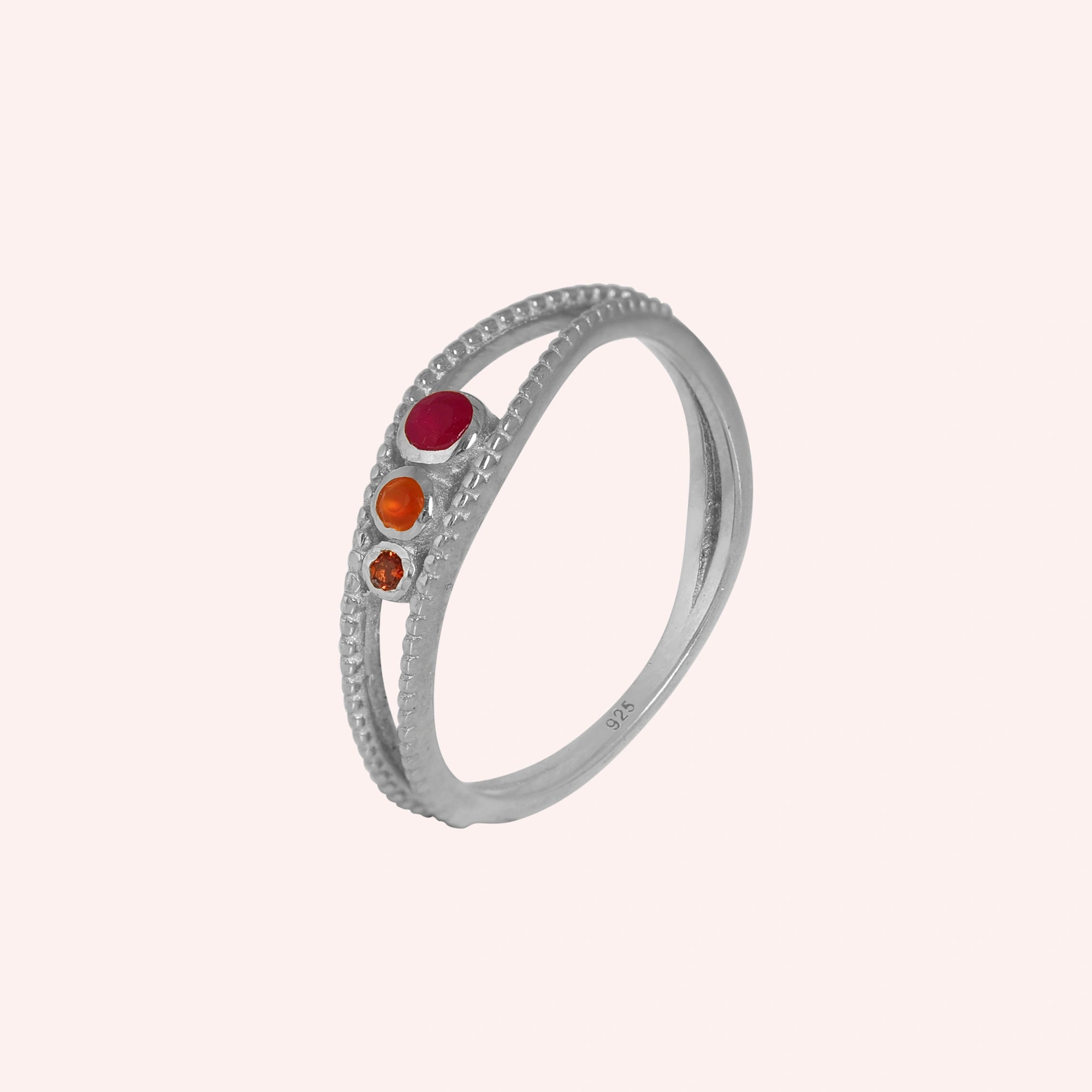 Three-stone-ring-in-sterling-silver-with-pink-red-and-orange-stones-in-angled-side-view-on-solid-pink-background