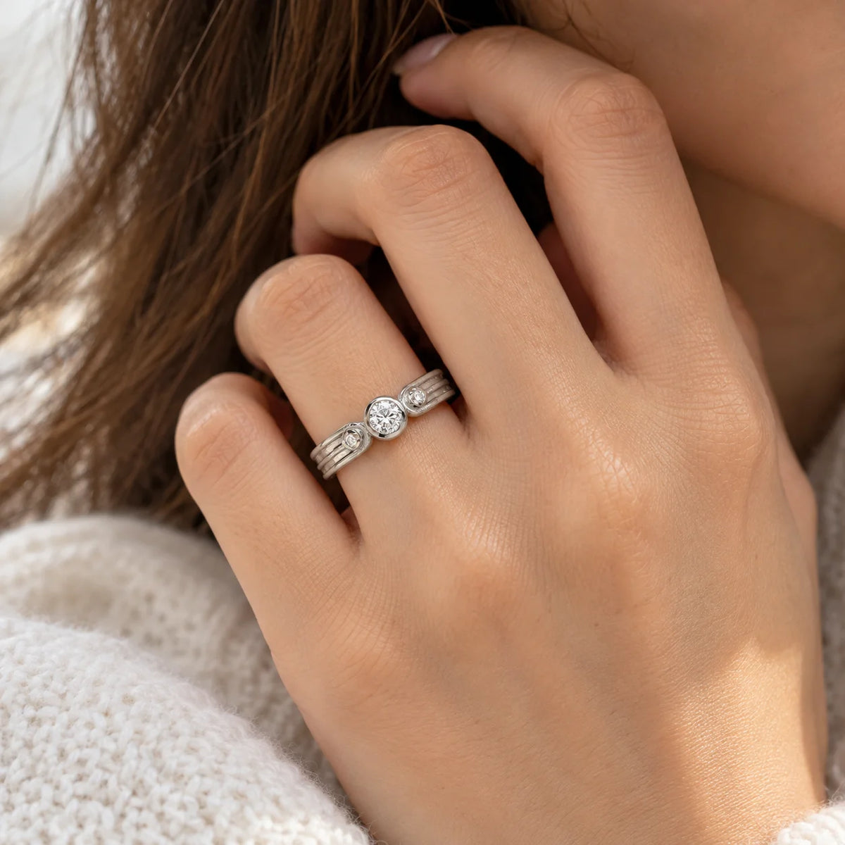 Three_stone_ring_in_sterling_silver_with_round_lab_grown_diamonds_at_front_angle_worn_by_a_model